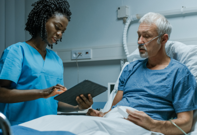 Un'infermiera con un tablet parla con un paziente anziano in ospedale.