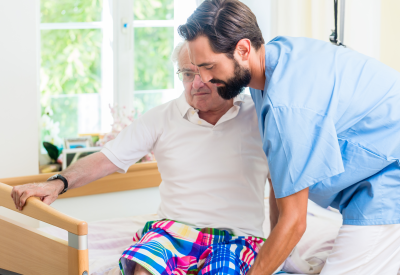 Un'infermiera geriatrica aiuta un uomo anziano ad alzarsi dalla sedia a rotelle per andare a letto