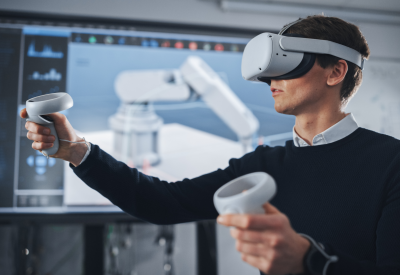 Studente ingegnere che indossa una cuffia per la realtà virtuale, tiene i joystick e controlla l'arto bionico mentre le azioni vengono visualizzate sullo schermo