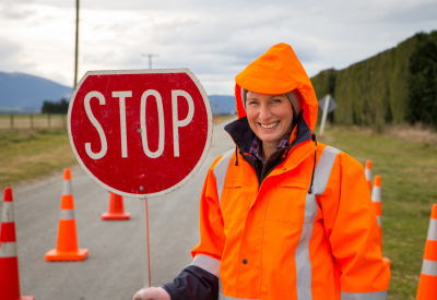 Una donna di una squadra stradale aziona un segnale di stop in un'area di pericolo su una strada rurale a Canterbury, in Nuova Zelanda.
