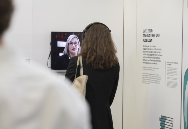 Donna con cuffie in piedi davanti a uno schermo della mostra «Al centro dell’apprendistato»