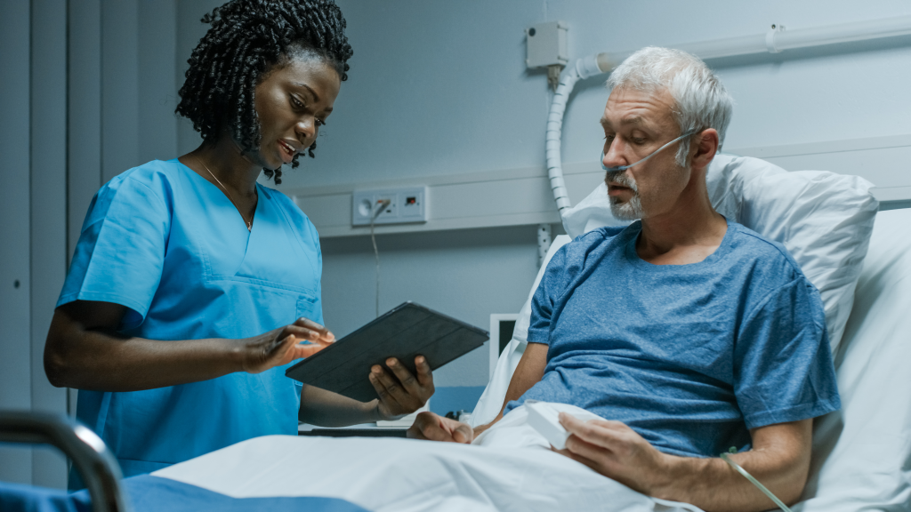 Un'infermiera con un tablet parla con un paziente anziano in ospedale.