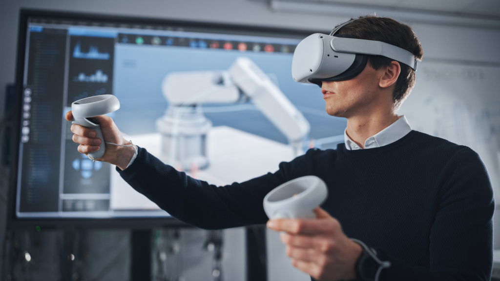 Studente ingegnere che indossa una cuffia per la realtà virtuale, tiene i joystick e controlla l'arto bionico mentre le azioni vengono visualizzate sullo schermo
