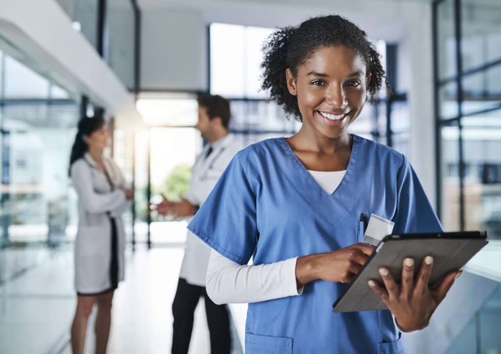 Le nostre cartelle cliniche sono tutte digitalizzate. Scatto di una giovane dottoressa che utilizza una tavoletta digitale in un ospedale, con i suoi colleghi sullo sfondo.